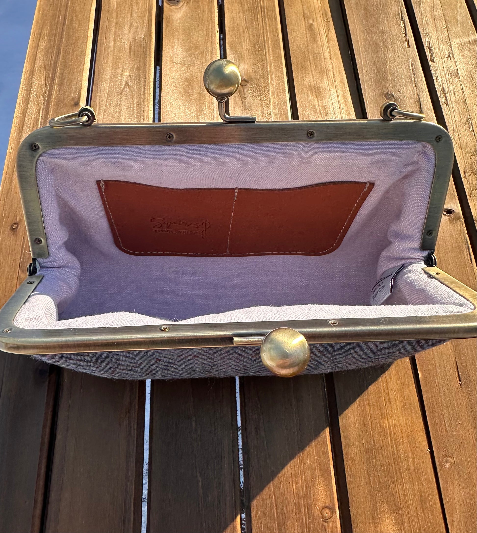 Interior of Blue Herringbone Harris Tweed® kiss lock purse. Lilac Linen lining complements tweed exterior. Bronze hardware, card slots, fits phone and small items.