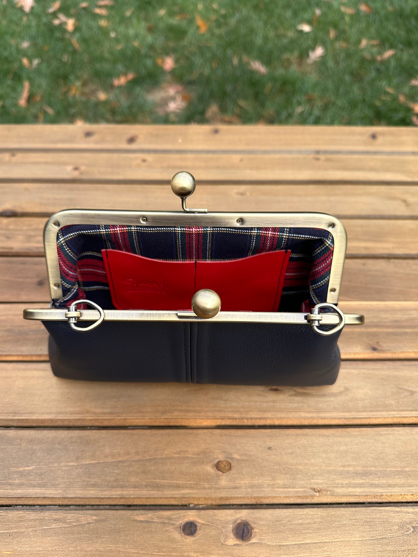 Interior of Navy leather kiss lock purse with Red Plaid lining. Includes 2 card slots and space for phone and essentials. Compact and functional design. Made in Maryland.