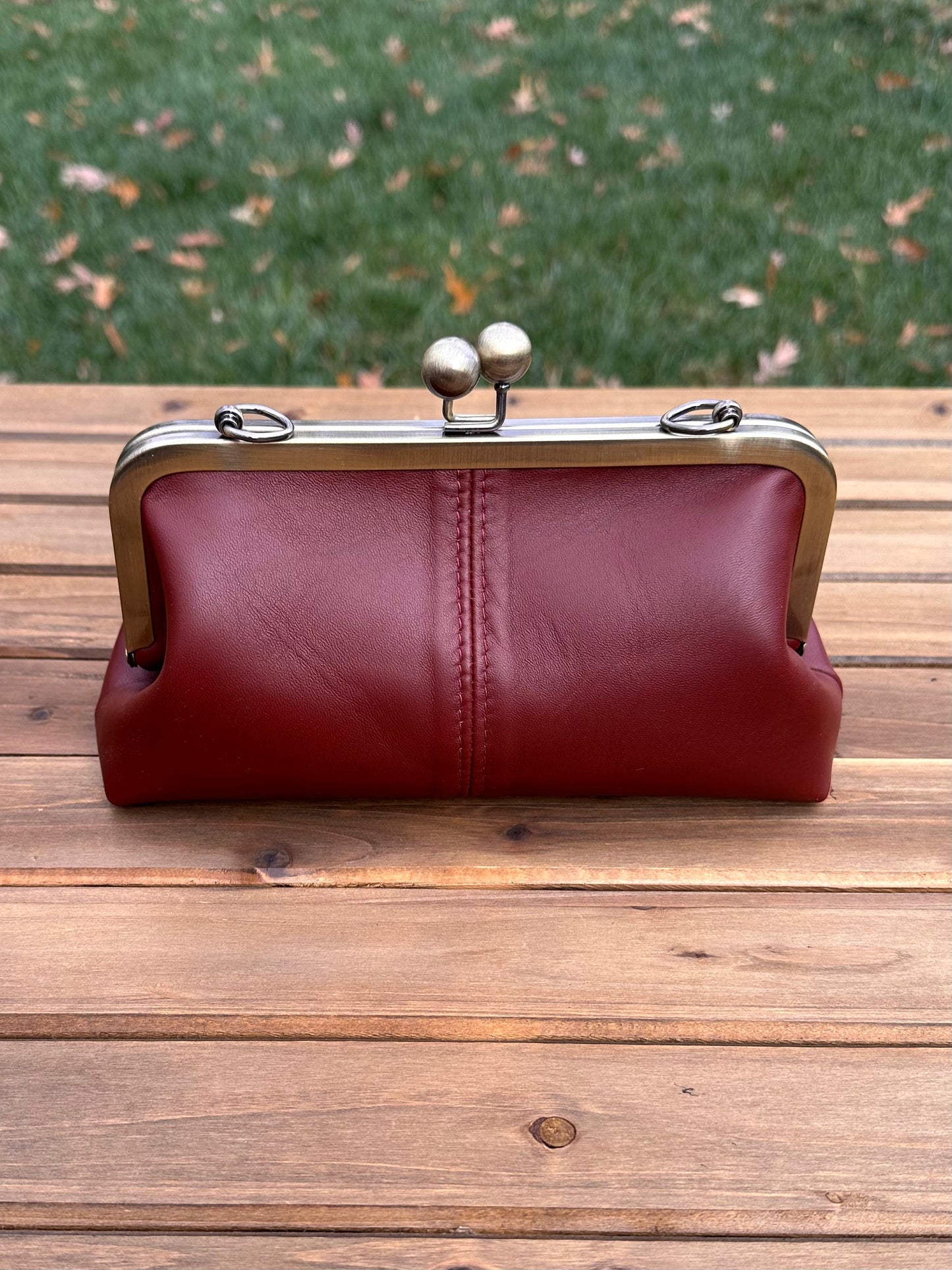 Leather kiss lock purse in Burgundy with bronze hardware. Wear as a clutch, crossbody, or shoulder bag. Holds phone, cards, and essentials. Made in Maryland.