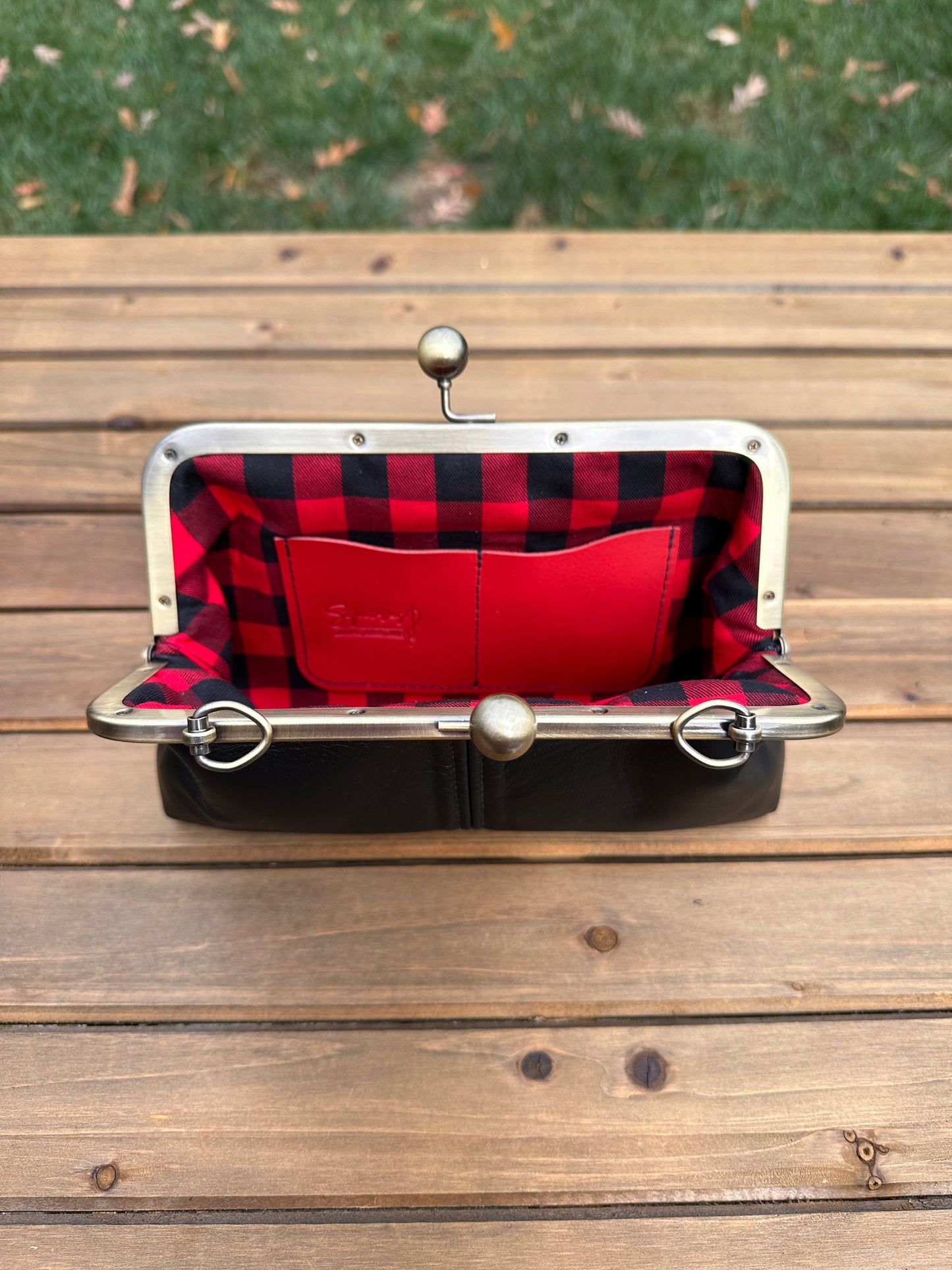 Interior of Black leather kiss lock purse with Red and Black Buffalo Plaid lining. Includes 2 card slots and space for phone and essentials. Compact and functional design. Made in Maryland.