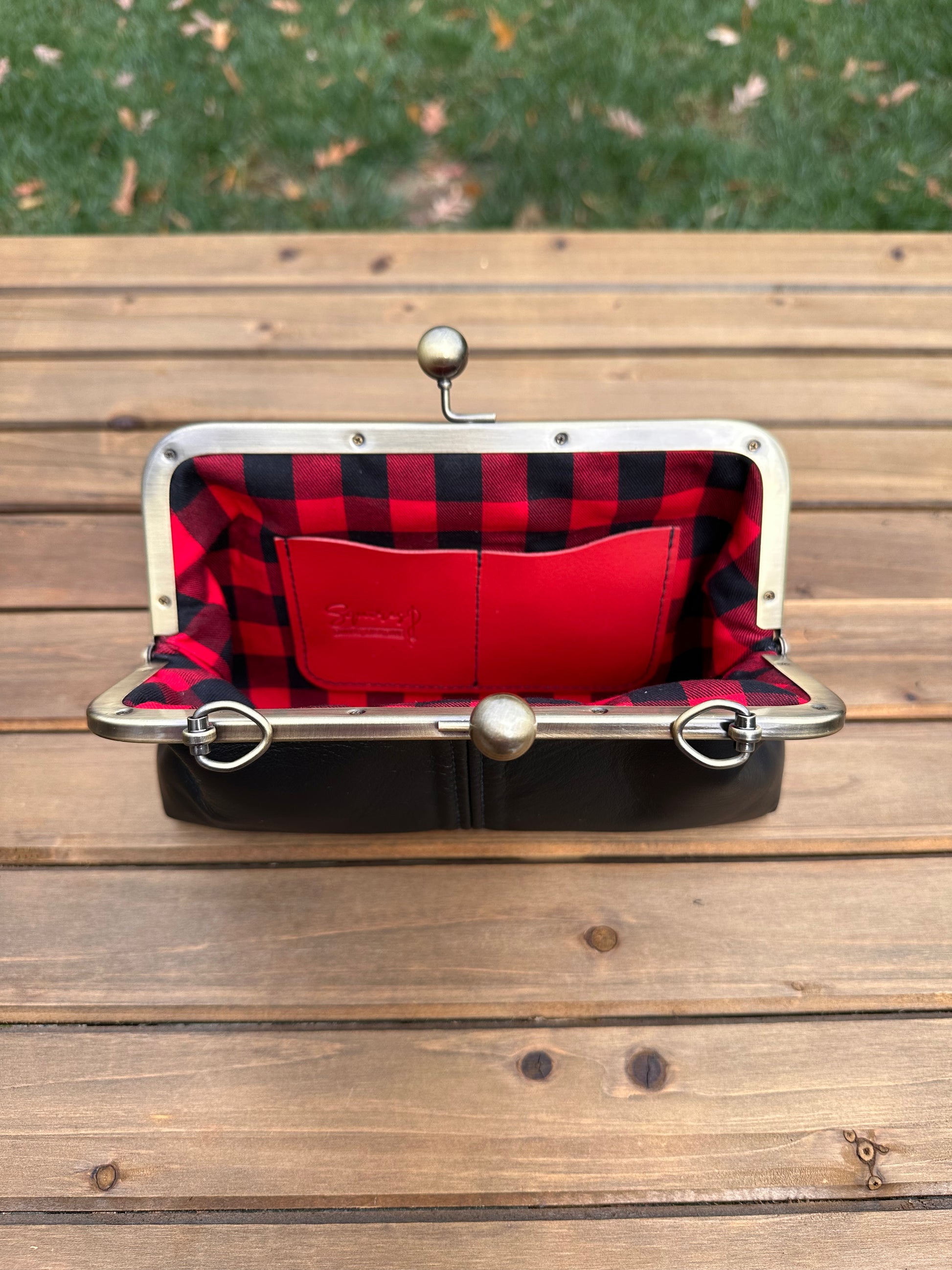 Interior of Black leather kiss lock purse with Red and Black Buffalo Plaid lining. Includes 2 card slots and space for phone and essentials. Compact and functional design. Made in Maryland.