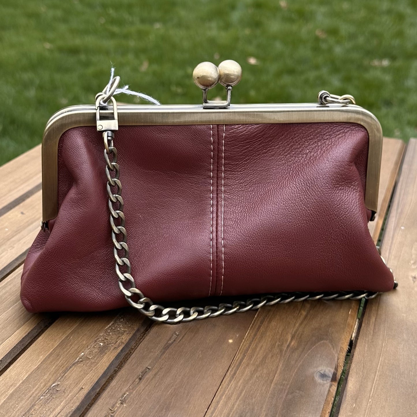 Leather kiss lock purse in Burgundy with bronze hardware. Wear as a clutch, crossbody, or shoulder bag. Holds phone, cards, and essentials. Made in Maryland.