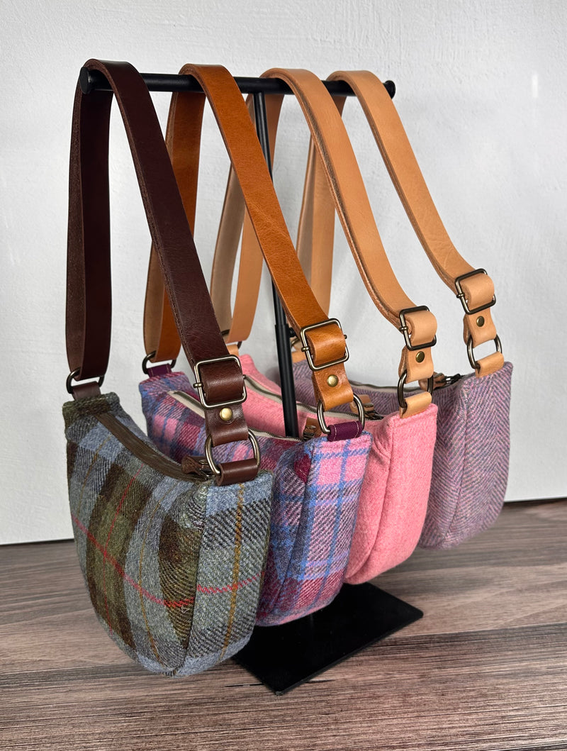 Set of four handcrafted Harris Tweed bags with leather straps on a stand against a white wall.