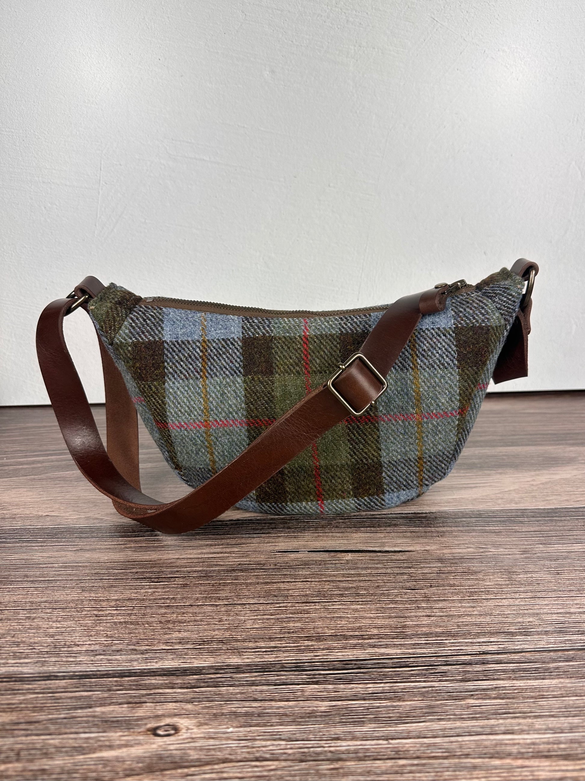 Handcrafted Harris Tweed Macleod Plaid half moon shaped bag with brown leather strap on a wooden surface
