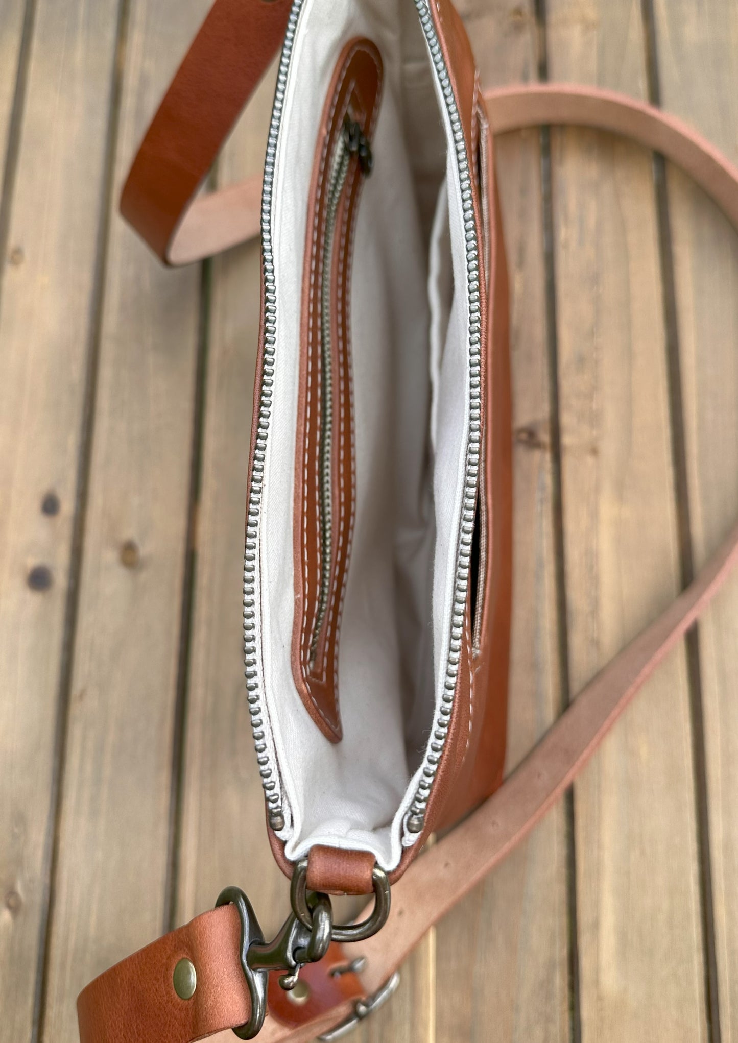 Overhead view of a opened handcrafted Leather Bayside Crossbody bag in Sienna Horween leather, showcasing its rich, warm color, natural grain, solid brass hardware, and full metal zipper. Designed and made in Maryland.