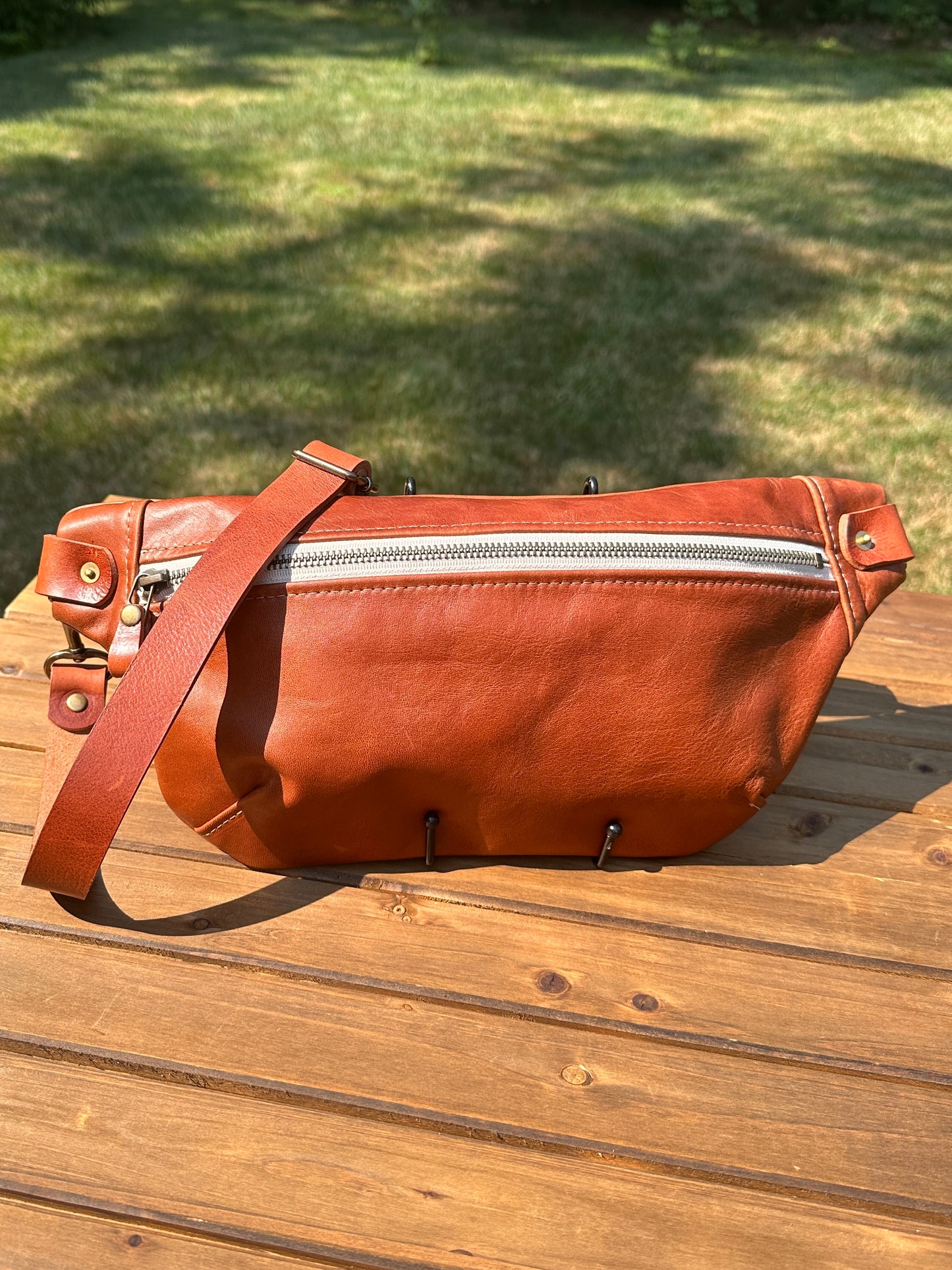 Front view of Leather Spinnaker Sling bag in Sienna with bronze hardware, linen interior, and front zipper. Unisex slim crossbody sling handmade in Maryland.