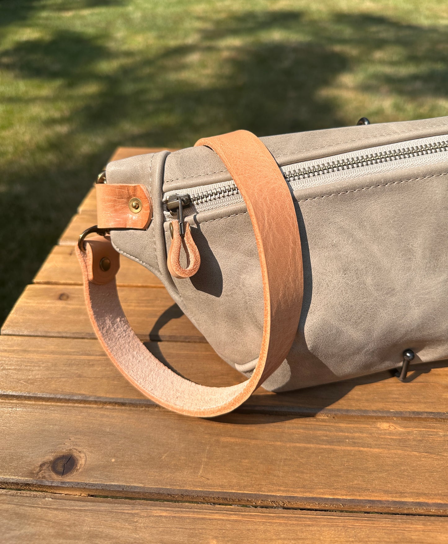 Close-up detail of the front zipper and grain texture on the Leather Spinnaker Sling in Distressed Gray, with solid brass hardware and full-grain leather. Handcrafted in Maryland.