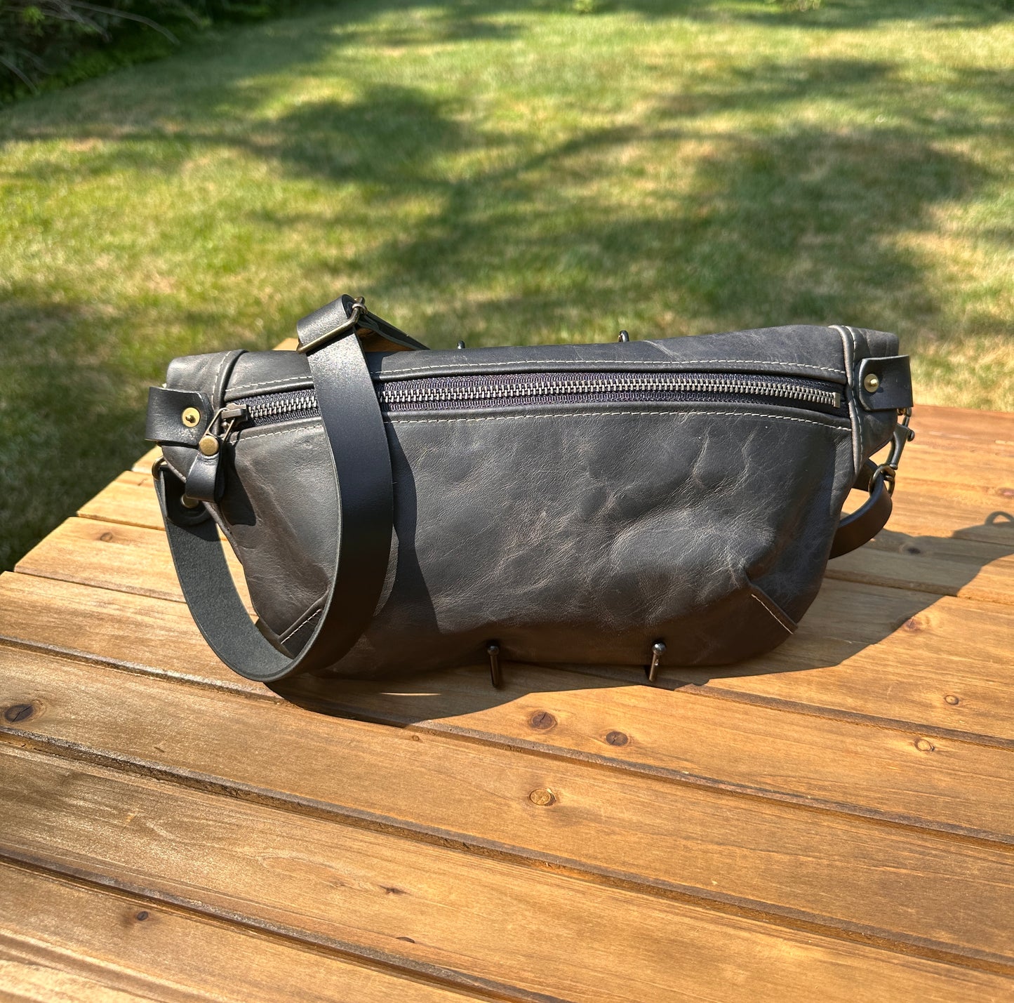 Front view of Leather Spinnaker Sling bag in Rustic Charcoal Dublin Leather with bronze hardware, linen interior, and front zipper. Unisex slim crossbody sling handmade in Maryland.