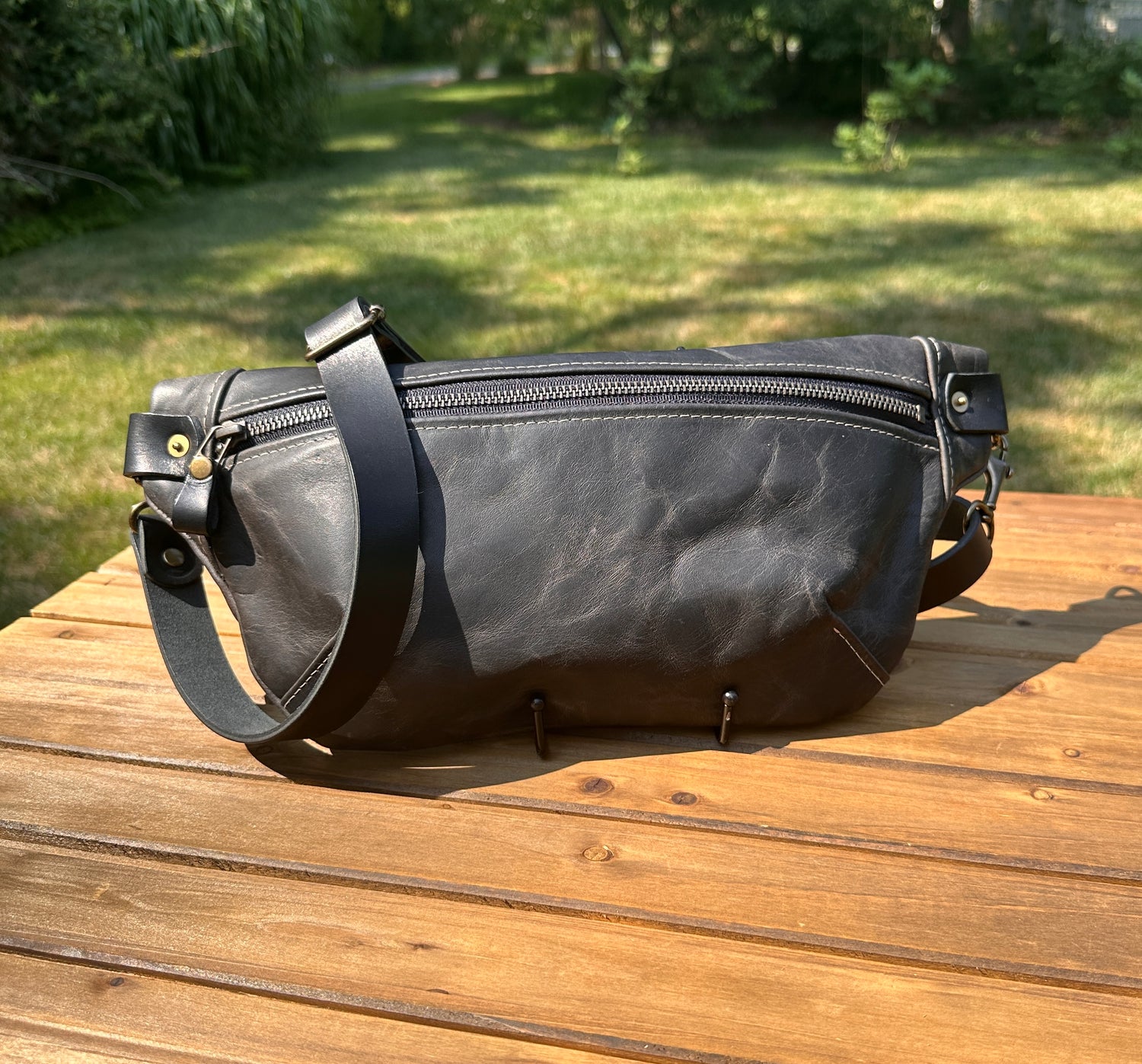 Front view of Leather Spinnaker Sling bag in Rustic Charcoal Dublin Leather with bronze hardware, linen interior, and front zipper. Unisex slim crossbody sling handmade in Maryland.