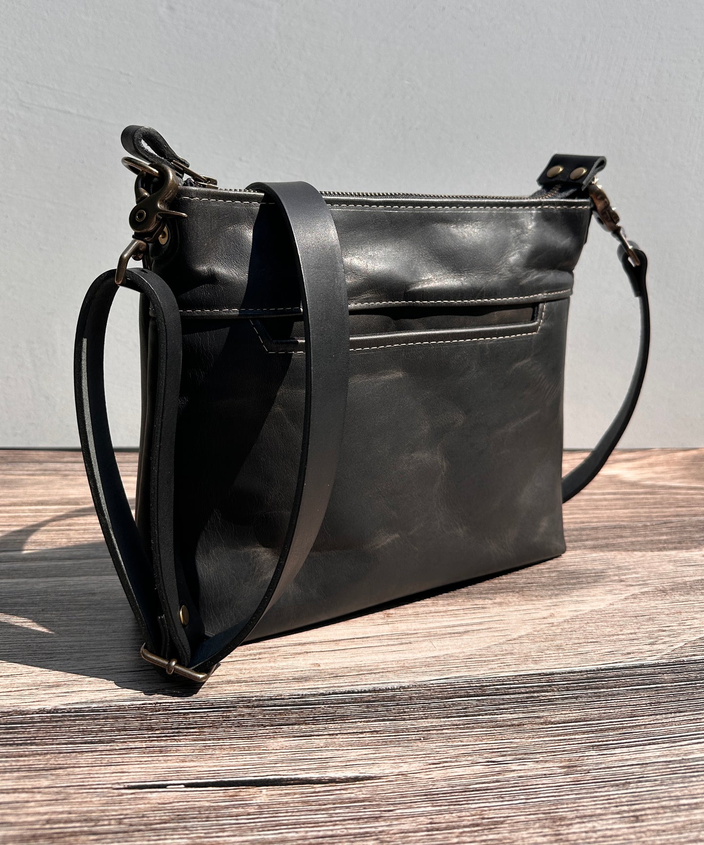 Front view of a handcrafted Leather Bayside Crossbody bag in Rustic Charcoal Horween leather, showcasing its rich, warm color, natural grain, solid brass hardware, and full metal zipper. Designed and made in Maryland.