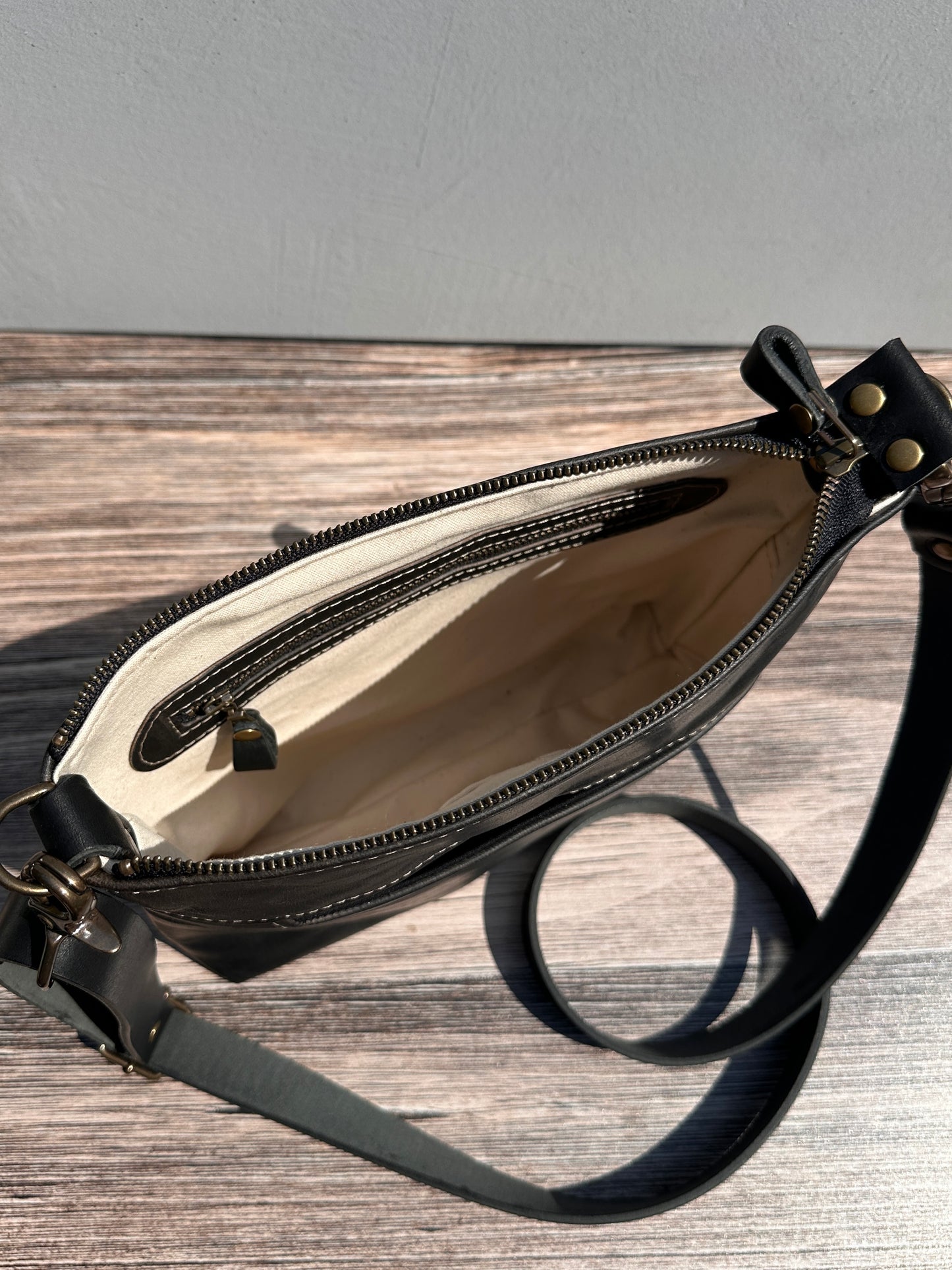 Overhead view of a opened handcrafted Leather Bayside Crossbody bag in Rustic Charcoal Horween leather, showcasing its rich, warm color, natural grain, solid brass hardware, and full metal zipper. Designed and made in Maryland.