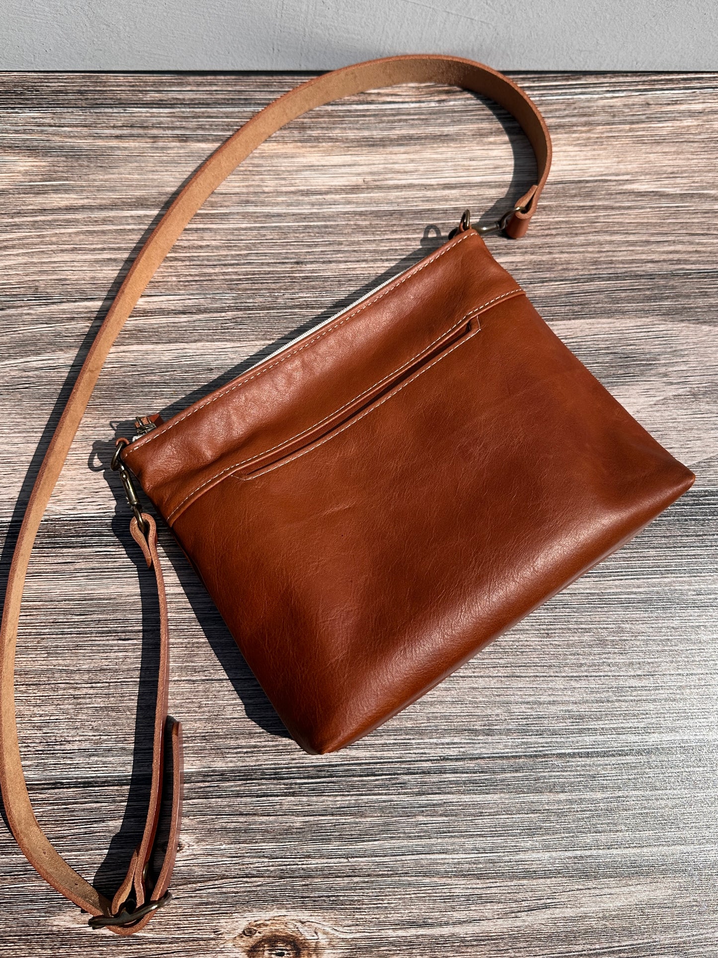 Overhead view of a handcrafted Leather Bayside Crossbody bag in Sienna Horween leather, showcasing its rich, warm color, natural grain, solid brass hardware, and full metal zipper. Designed and made in Maryland.
