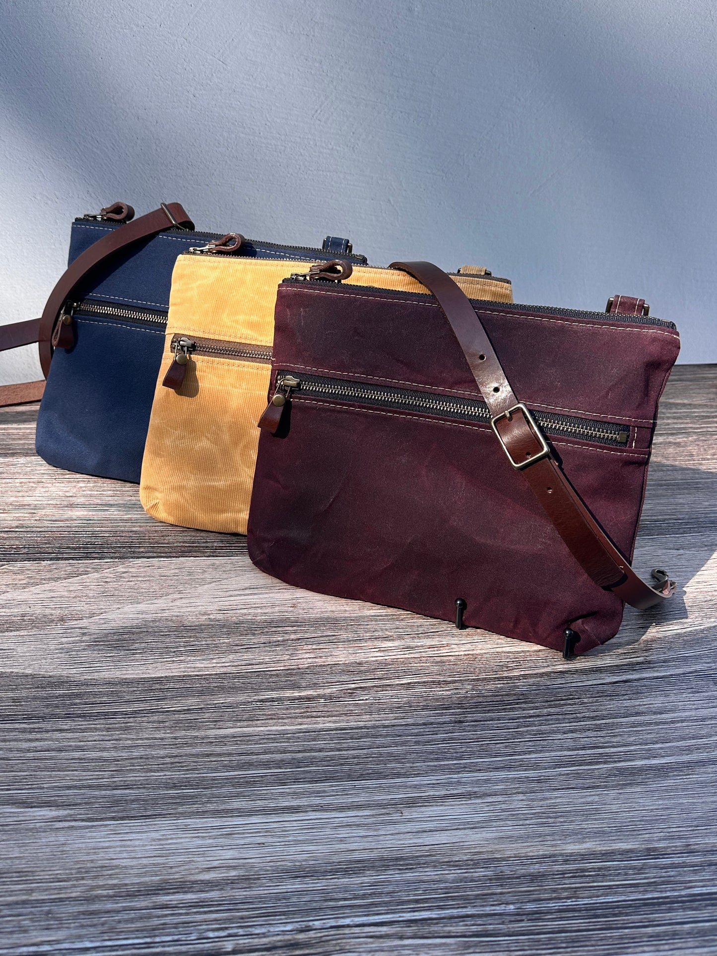 Collection of handcrafted Canvas Bayside Slim Crossbody Bags in waxed canvas, and solid canvas styles, with full canvas lining and adjustable vegetable-tanned leather straps.