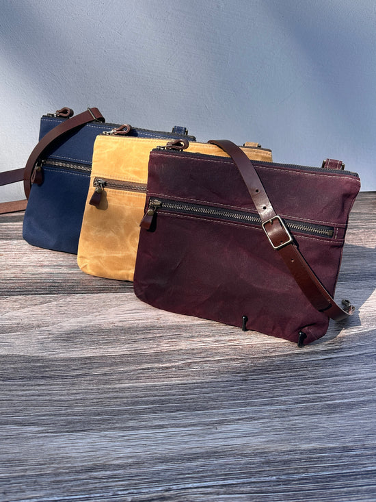 Collection of handcrafted Canvas Bayside Slim Crossbody Bags in waxed canvas, and solid canvas styles, with full canvas lining and adjustable vegetable-tanned leather straps.