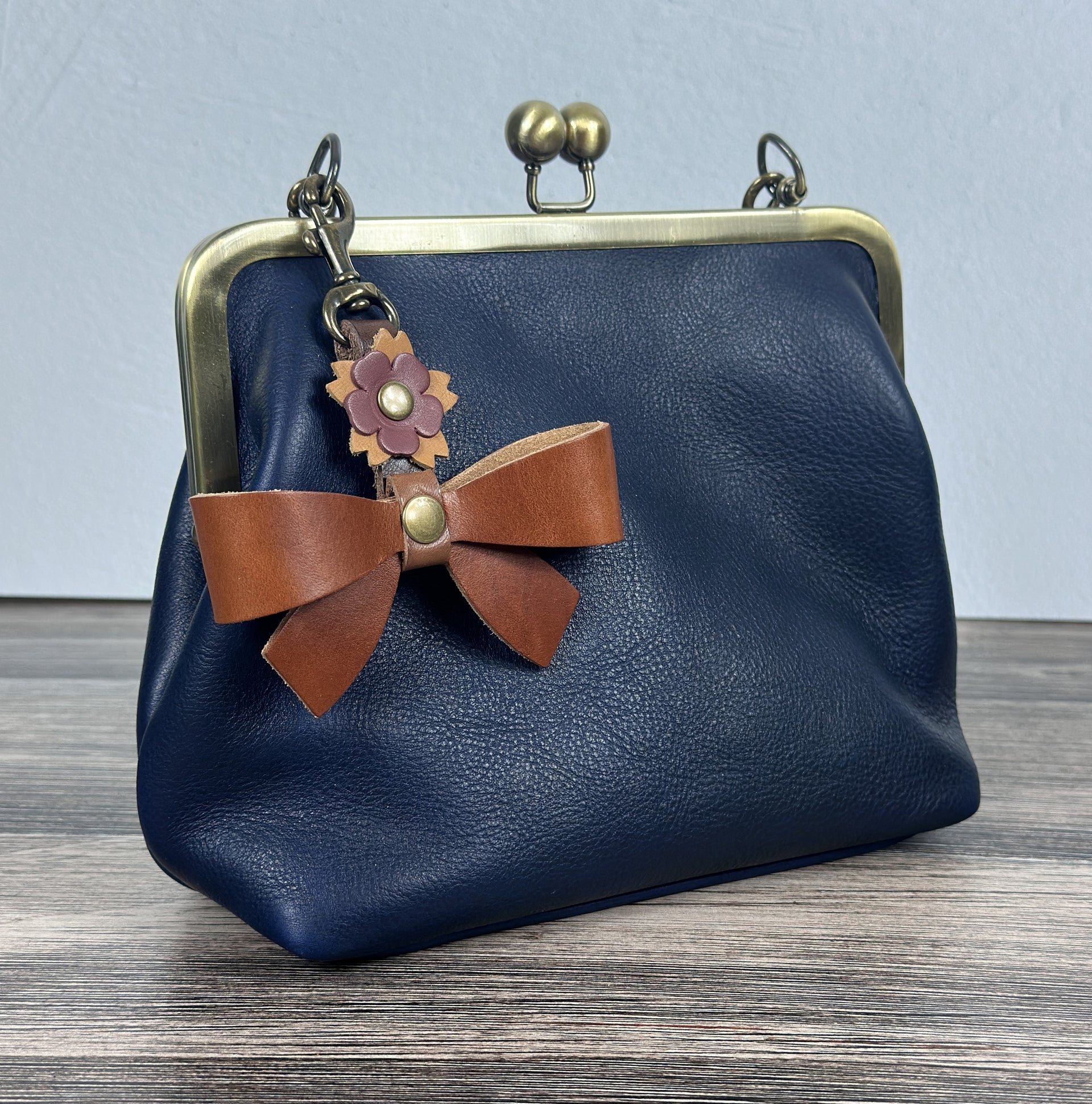Handcrafted full-grain leather Princess Anne Kiss Lock handbag featuring a vintage-style frame and convertible straps with a leather trinket Bow Charm.