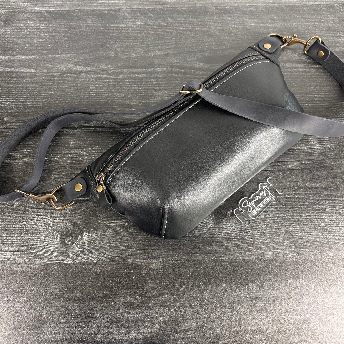 Side view of Leather Spinnaker Sling bag in Black with bronze hardware, Wickett & Craig Black English Bridle Leather Strap, and front zipper. Unisex slim crossbody sling handmade in Maryland.