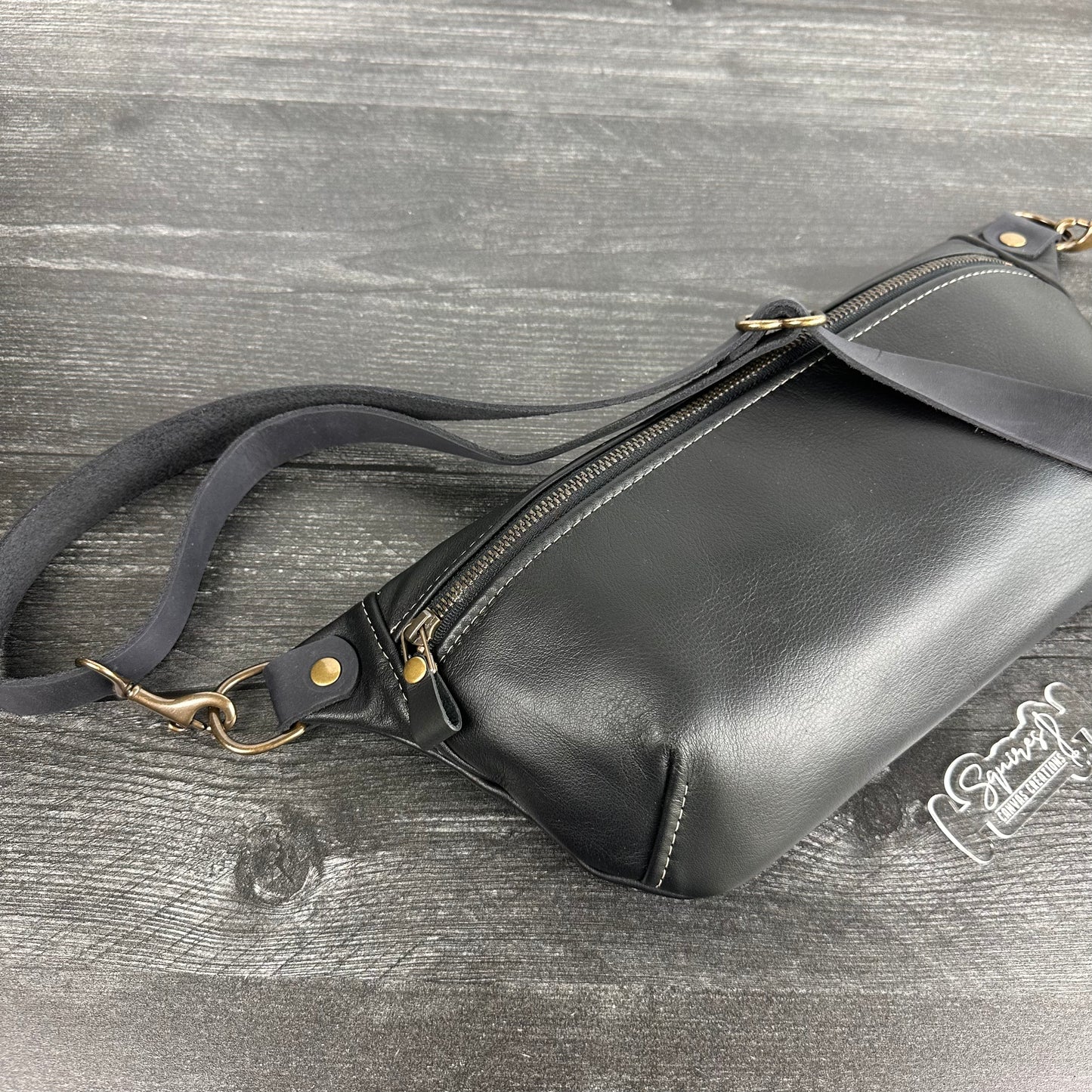 Side view of Leather Spinnaker Sling bag in Black with bronze hardware, Wickett & Craig Black English Bridle Leather Strap, and front zipper. Unisex slim crossbody sling handmade in Maryland.