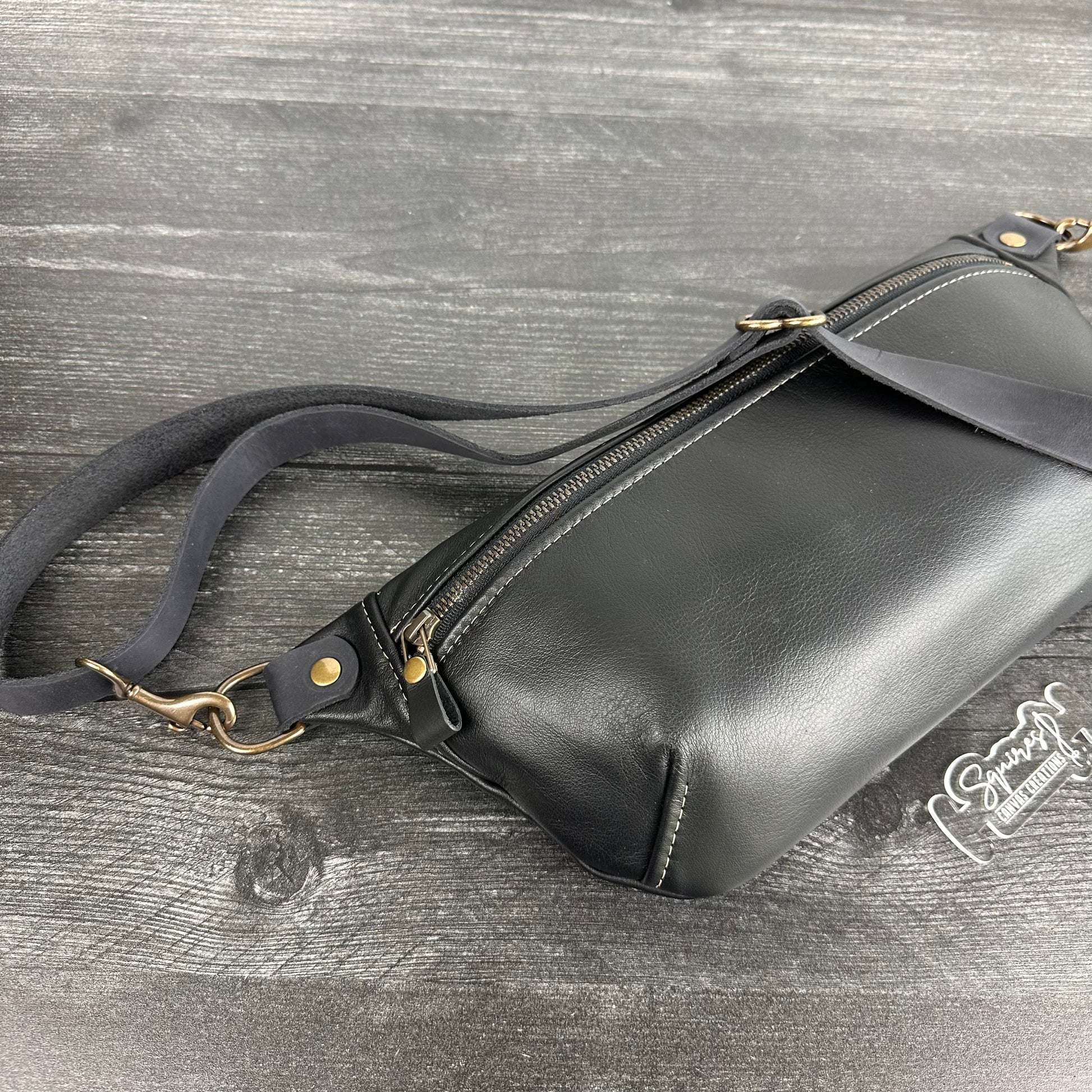 Side view of Leather Spinnaker Sling bag in Black with bronze hardware, Wickett & Craig Black English Bridle Leather Strap, and front zipper. Unisex slim crossbody sling handmade in Maryland.