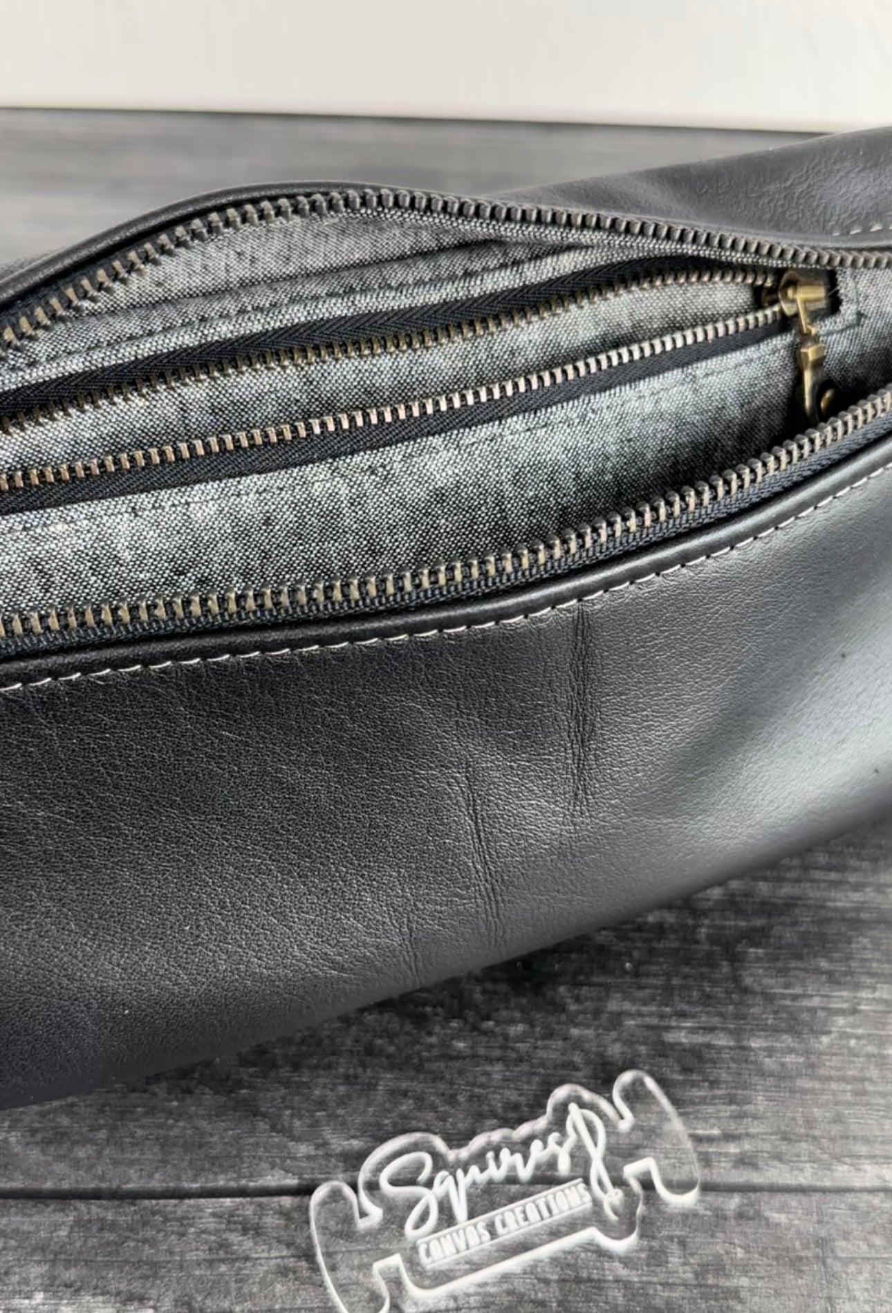 Side view of Leather Spinnaker Sling bag in Black with bronze hardware, Grey linen interior, interior Zipper, and front zipper. Unisex slim crossbody sling handmade in Maryland.