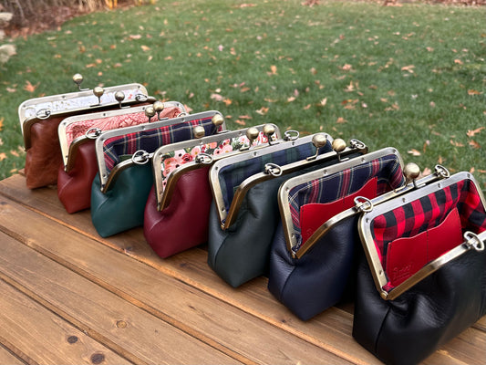 Collection of handcrafted leather kiss lock purses with bronze hardware and chain straps.  The interior of leather kiss lock purses with various colorful linings. Includes 2 card slots and space for phone and essentials. Compact and functional design. Wear as clutch, shoulder, or crossbody. Made in Maryland.