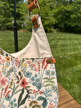 Close up detail view of the Compass Rose Shoulder bag in Rifle Paper Co. Herb Garden Natural Canvas with Cognac Leather.  The detailed view shows the leather strap connector and riveted leather corner detail.