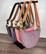 Set of four handcrafted Harris Tweed bags with different color leather straps on a stand against a white wall.
