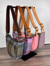 Set of four handcrafted Harris Tweed bags with leather straps on a stand against a white wall.