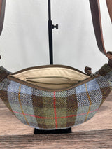 An open view of the Harris Tweed Macleod Plaid half moon shaped bag with brown leather strap on stand