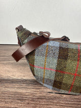 Close up Harris Tweed Macleod Plaid half moon shaped bag with brown leather strap on a wooden surface