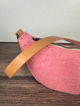 Close up of Pink Harris Tweed half moon circle sling with a natural leather strap on a wooden surface