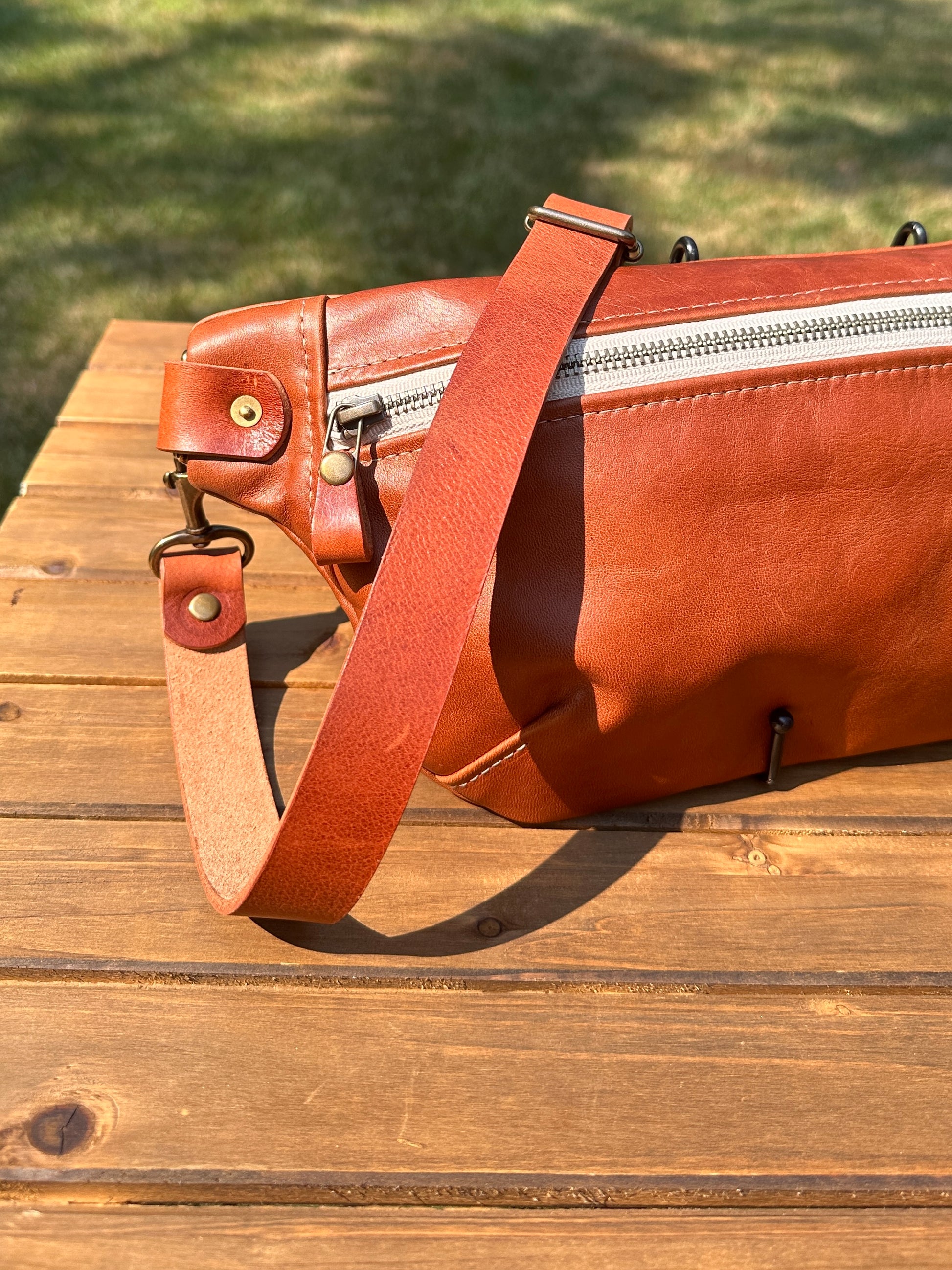 Close-up detail of the front zipper and grain texture on the Leather Spinnaker Sling in Sienna, with solid brass hardware and full-grain leather. Handcrafted in Maryland.
