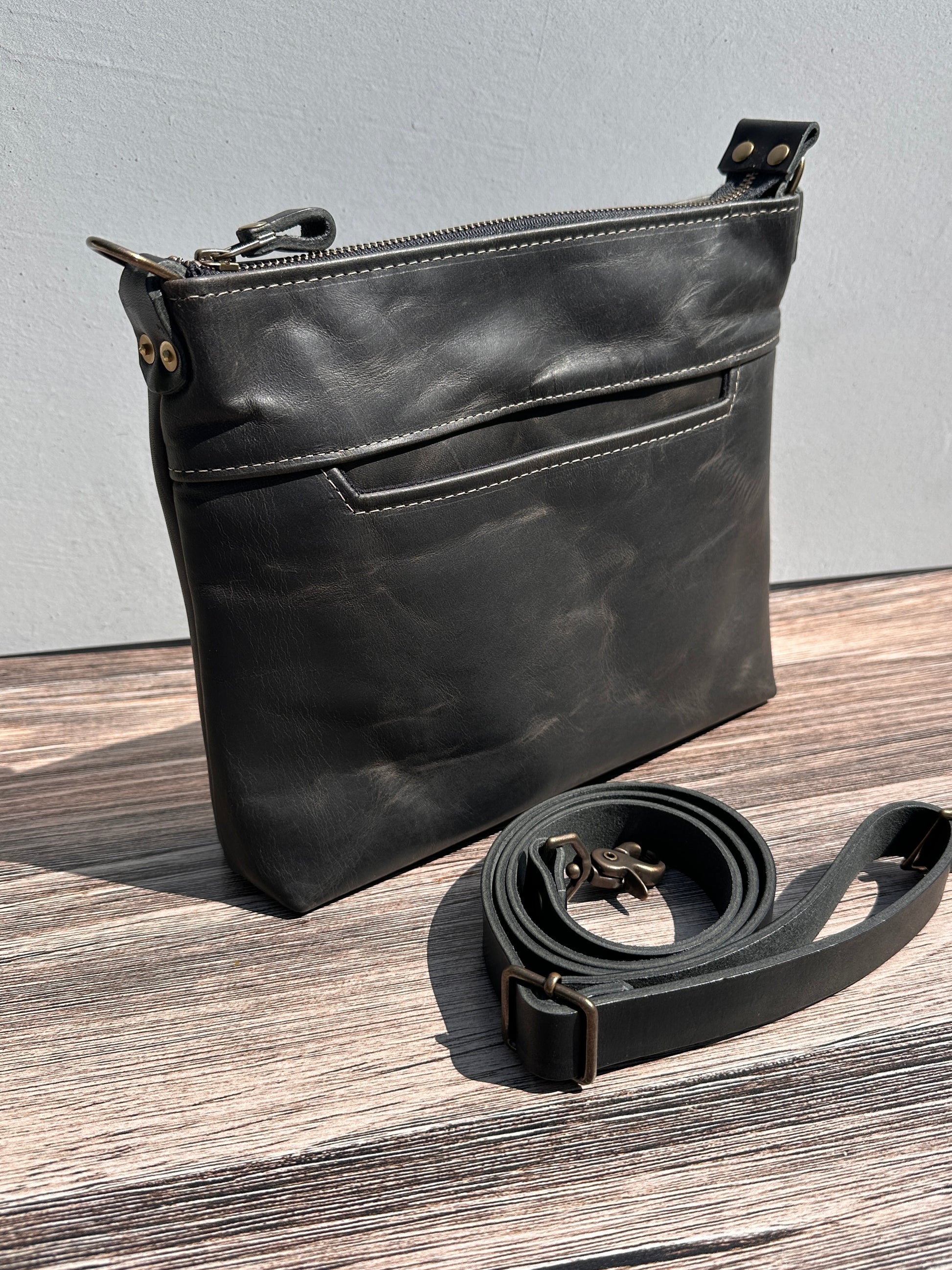 Front view of a handcrafted Leather Bayside Crossbody bag in Rustic Charcoal Horween leather, showcasing its rich, warm color, natural grain, solid brass hardware, and full metal zipper. Designed and made in Maryland.