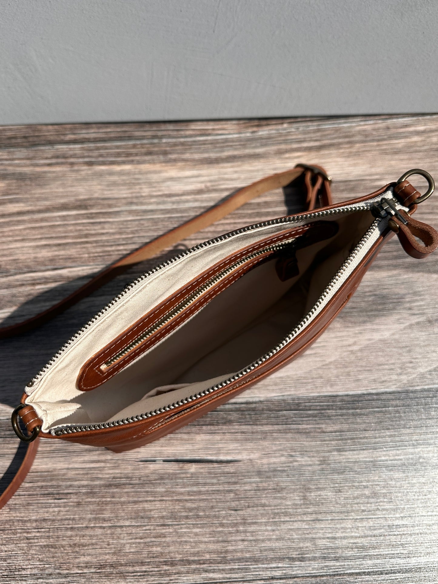 Overhead view of a opened handcrafted Leather Bayside Crossbody bag in Sienna Horween leather, showcasing its rich, warm color, natural grain, solid brass hardware, and full metal zipper. Designed and made in Maryland.
