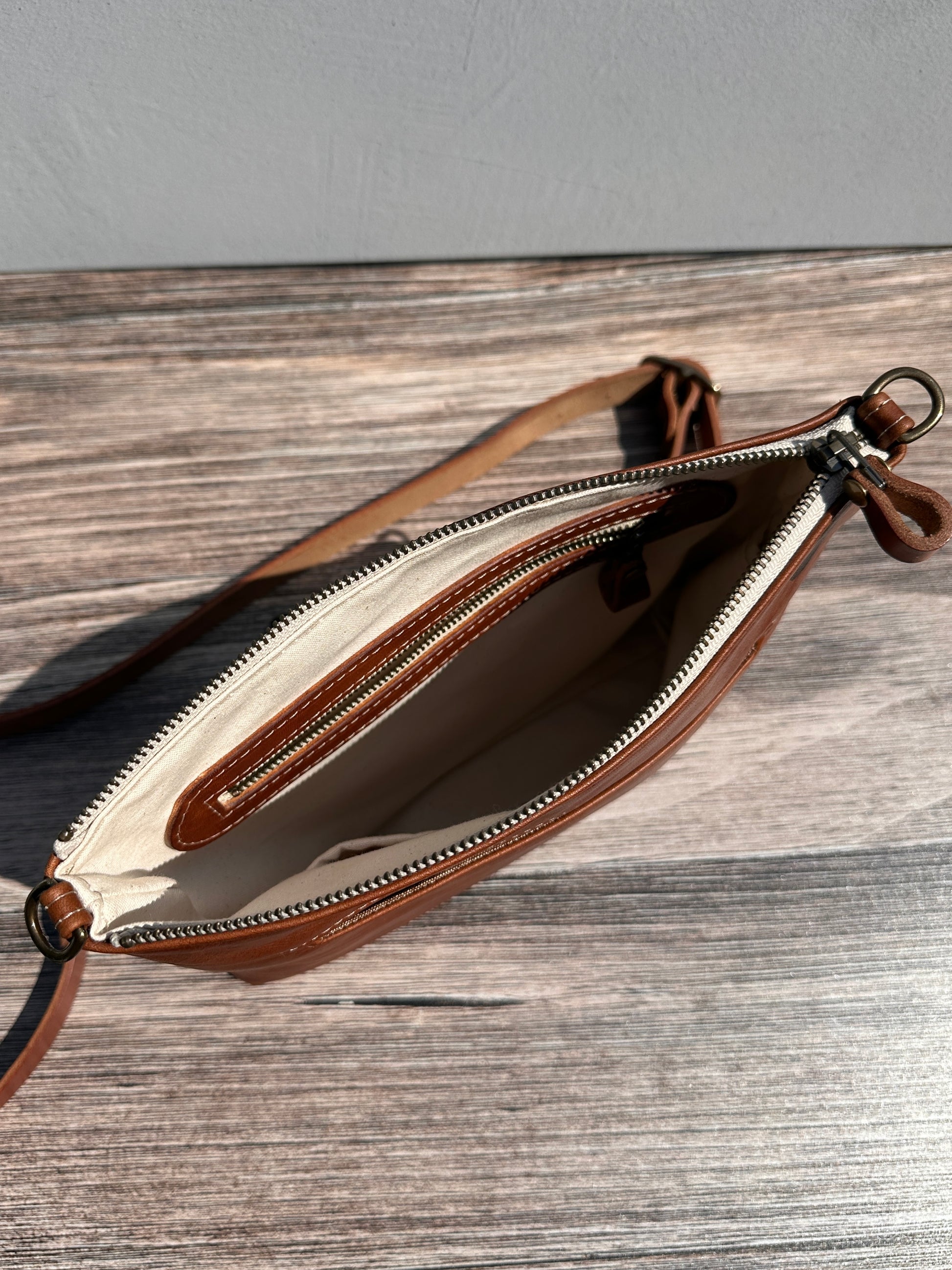 Overhead view of a opened handcrafted Leather Bayside Crossbody bag in Sienna Horween leather, showcasing its rich, warm color, natural grain, solid brass hardware, and full metal zipper. Designed and made in Maryland.