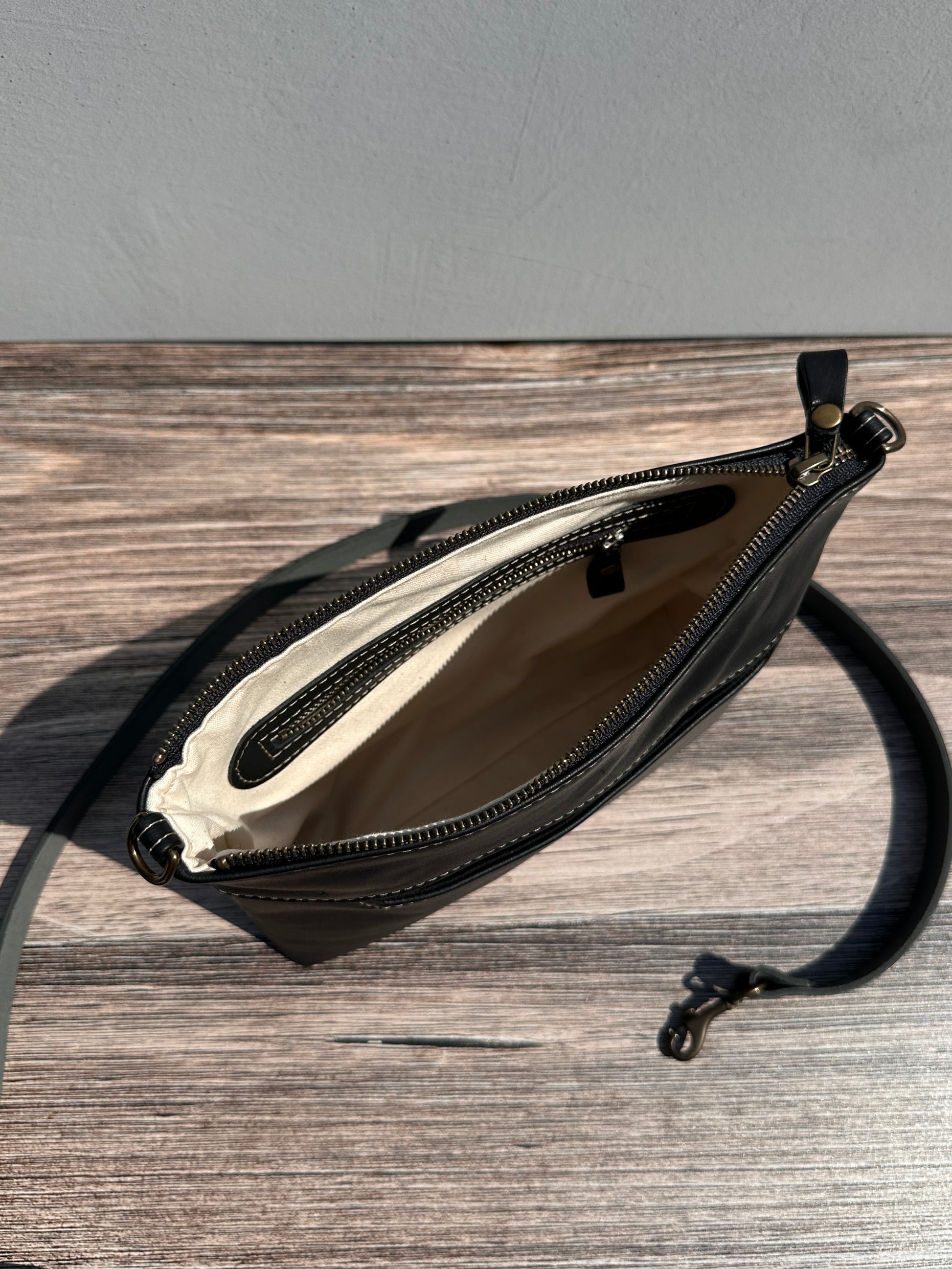Overhead view of a opened handcrafted Leather Bayside Crossbody bag in Bomber Jacket Black Horween leather, showcasing its rich, warm color, natural grain, solid brass hardware, and full metal zipper. Designed and made in Maryland.