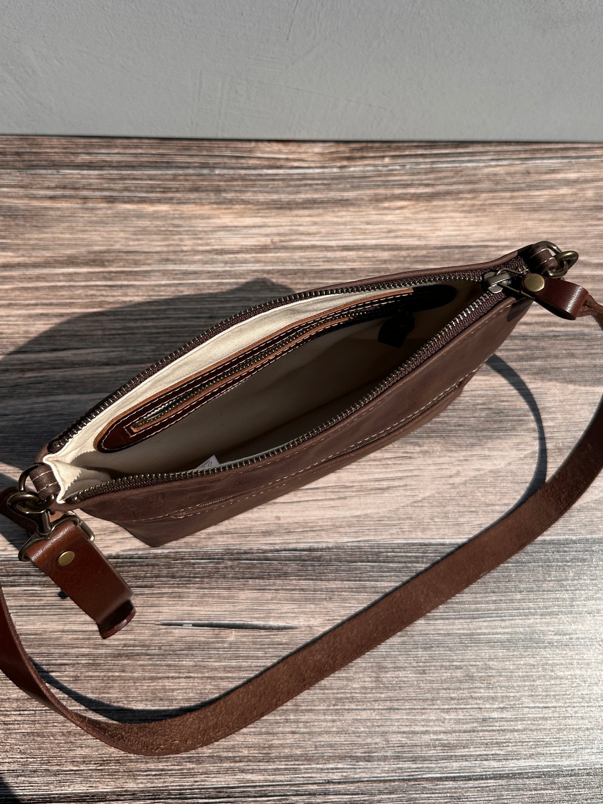 Overhead view of a opened handcrafted Leather Bayside Crossbody bag in Vintage Dark Brown Horween leather, showcasing its rich, warm color, natural grain, solid brass hardware, and full metal zipper. Designed and made in Maryland.