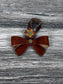 Cognac Leather bow purse charm with snap closure styled on a leather shoulder bag.