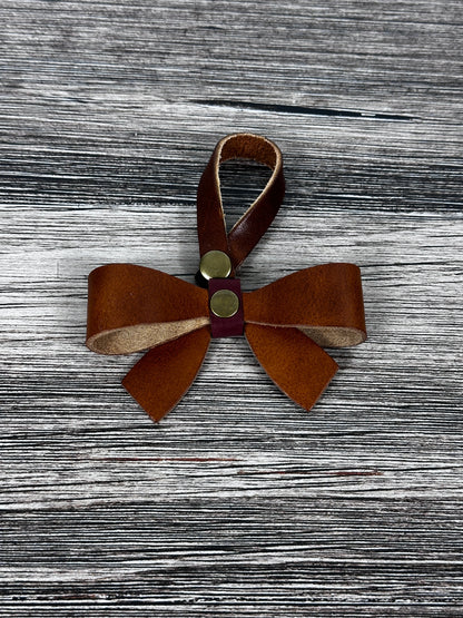 Leather bow purse charm with snap closure styled on a leather shoulder bag.