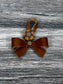 Cognac Leather bow purse charm with snap closure styled on a leather shoulder bag.