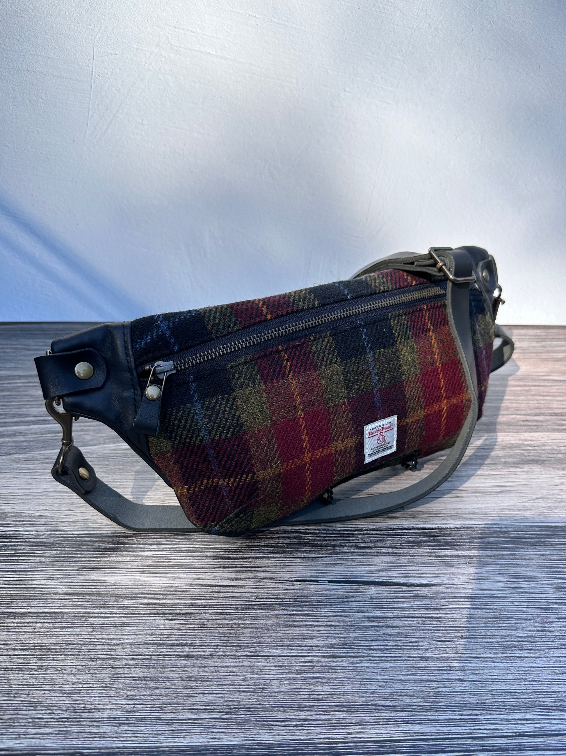Minimalist sling bag handcrafted with Green, Red, Black plaid Harris Tweed® and Horween Black Leather, finished with Antique Brass hardware.