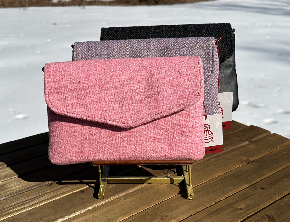 A collection of handcrafted Skye Fold clutches featuring authentic Harris Tweed flaps in pink, lilac herringbone and Black Harris Tweed with Leather patterns. These elegant envelope clutches showcase a refined contrast between premium leather bodies and heritage Scottish wool.