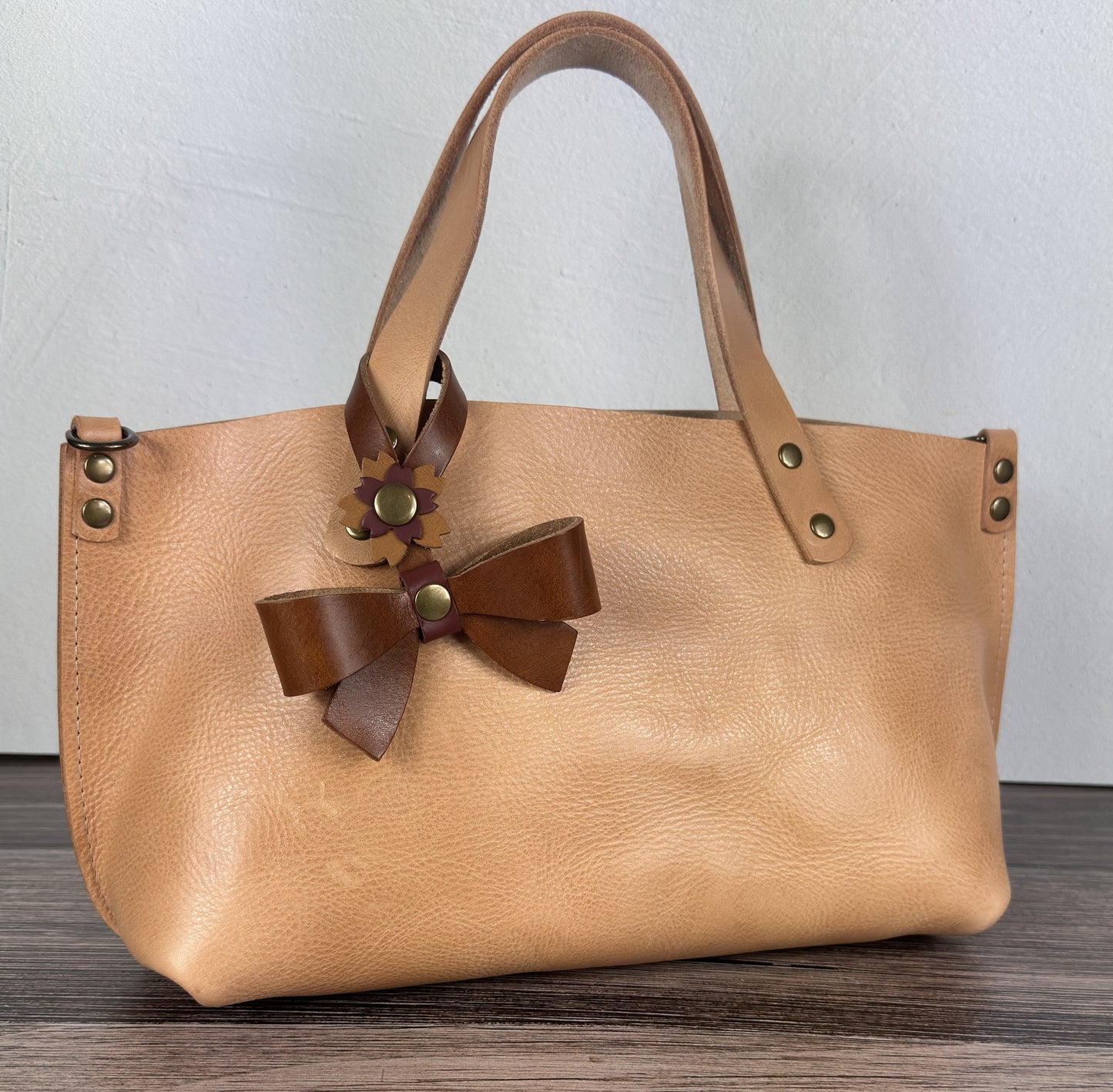 Leather bow bag charm clipped to a Leather Tote Handle – handcrafted purse accessory cut by hand.