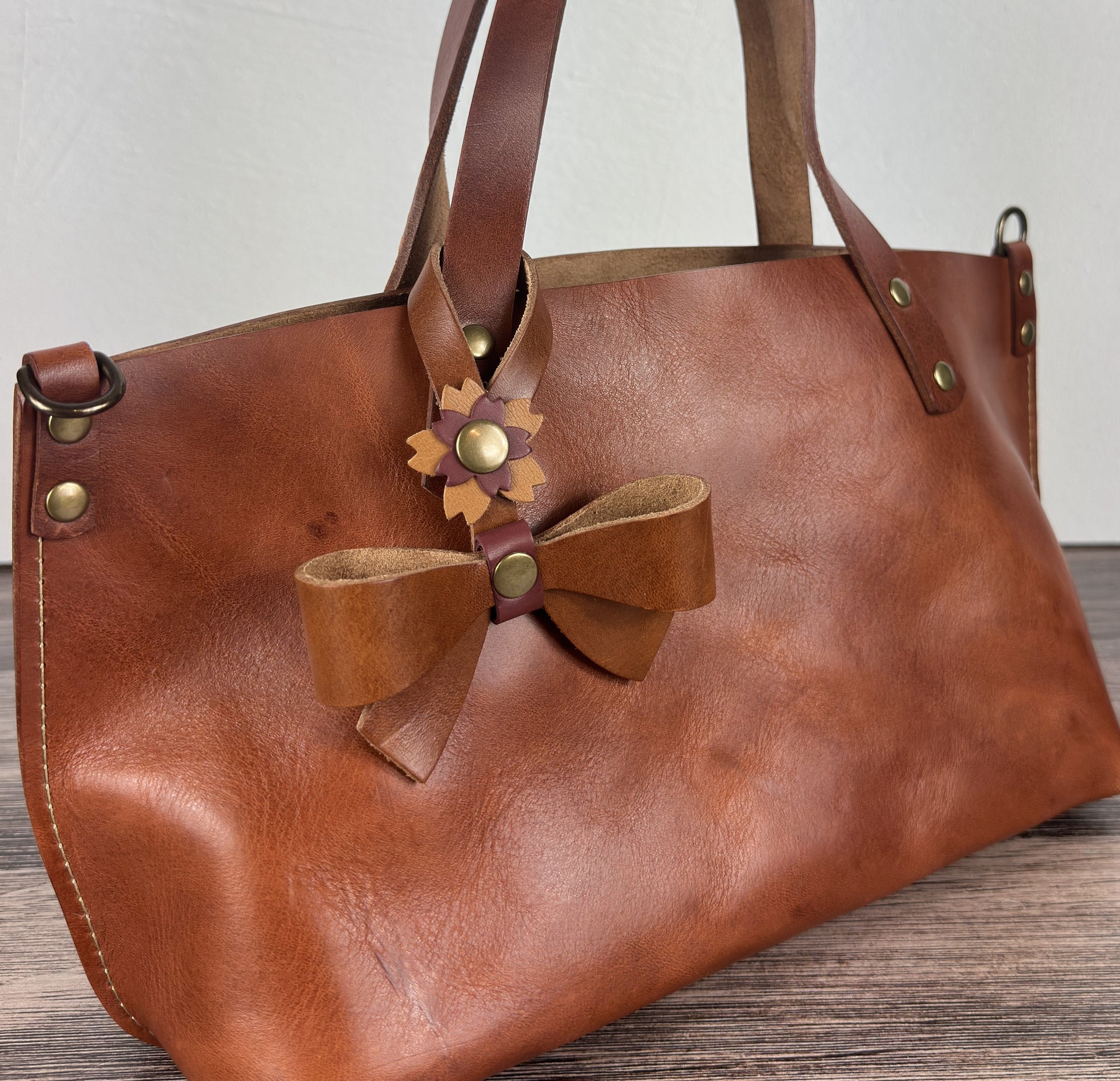 Leather bow bag charm clipped to a Leather Tote Handle – handcrafted purse accessory cut by hand.