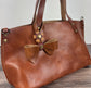 Leather bow bag charm clipped to a Leather Tote Handle – handcrafted purse accessory cut by hand.