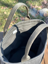 Large olive green heavy-duty canvas garden tool bag on its side showing the handles.  Close-up of the exterior slip pockets on a canvas bucket bag. Shows the heavy-duty stitching and reinforced construction ideal for organizing garden tools or daily essentials.  The Waterman Bucket Bag has four deep exterior pockets holding seed packets. Features durable webbing grab handles and a structured round base for upright utility.