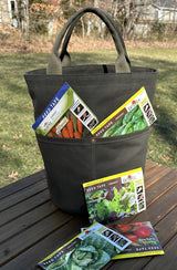 Waterman Bucket in olive green canvas bucket tote sitting on a wooden bench, functioning as a garden tool organizer. High-impact utility bag for home gardeners and hobbyists seeking durable handmade gear.