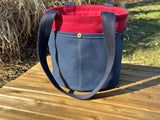 Side view of the Waterman Bucket Shorty is a small navy blue and red canvas bucket tote with long webbing shoulder straps. Shows the heavy-duty stitching and reinforced construction ideal for beach or pool bag handcrafted from 18oz cotton duck canvas for a classic nautical aesthetic.