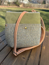 The Barra crossbody bag displayed with its natural leather strap and authentic Harris Tweed tag. A premium "slow fashion" accessory combining Scottish heritage textiles with rugged British waxed canvas.