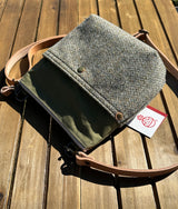 The Barra crossbody bag displayed with its natural leather strap and authentic Harris Tweed tag. A premium "slow fashion" accessory combining Scottish heritage textiles with rugged British waxed canvas.