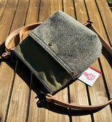 Barra hybrid bag in Barleycorn Harris Tweed and olive waxed canvas on a wooden table. Features an authentic Harris Tweed orb luxury label and a hand-cut natural leather shoulder strap.